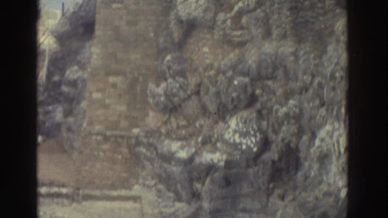 High-angle view of stone ruins and a narrow path, partly obscured by dark film-frame borders.