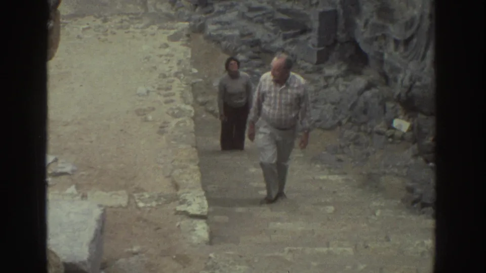 1976 Greece 8mm frame showing adult visitors moving through a narrow archaeological ruin passage.