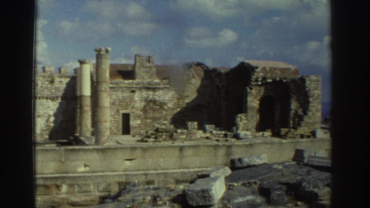 A handheld 1976 Greece view shows ancient stone walls, standing columns, and broken masonry beneath a partly cloudy sky.