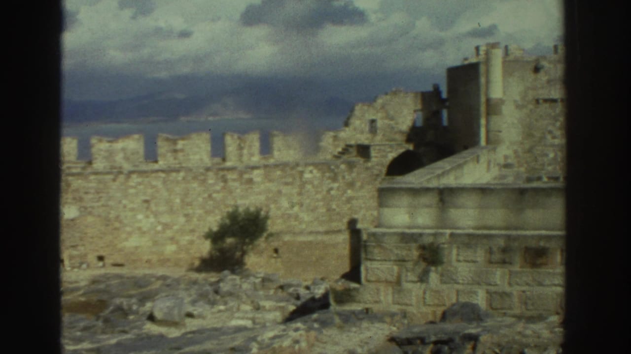 Stone fort wall, tower ruins, and rocky foreground with cloudy sky beyond.