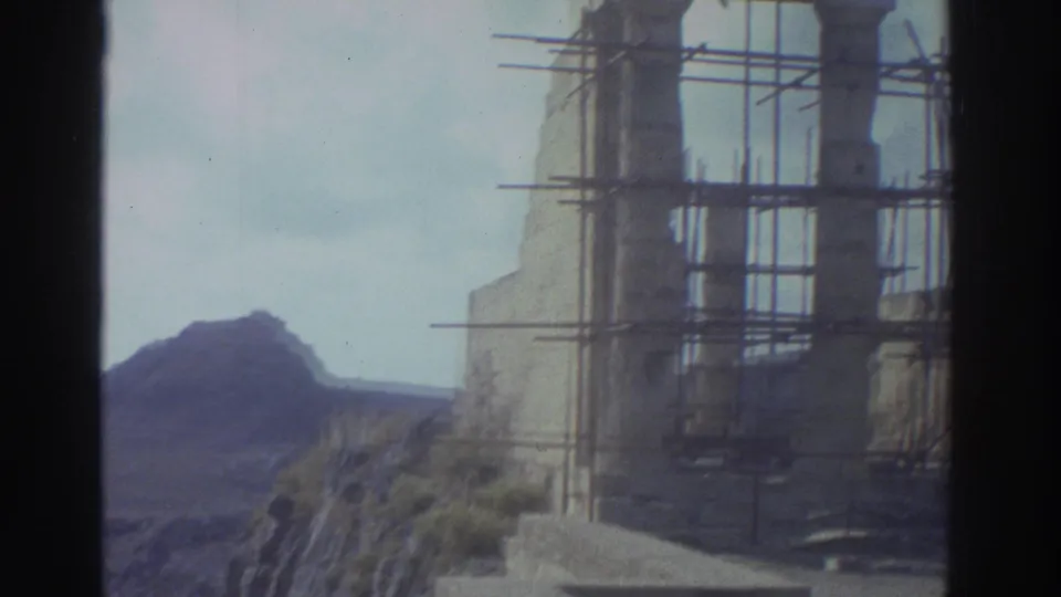 1976 Greece 8mm frame showing scaffolding around ancient stone columns near a coastal hillside.