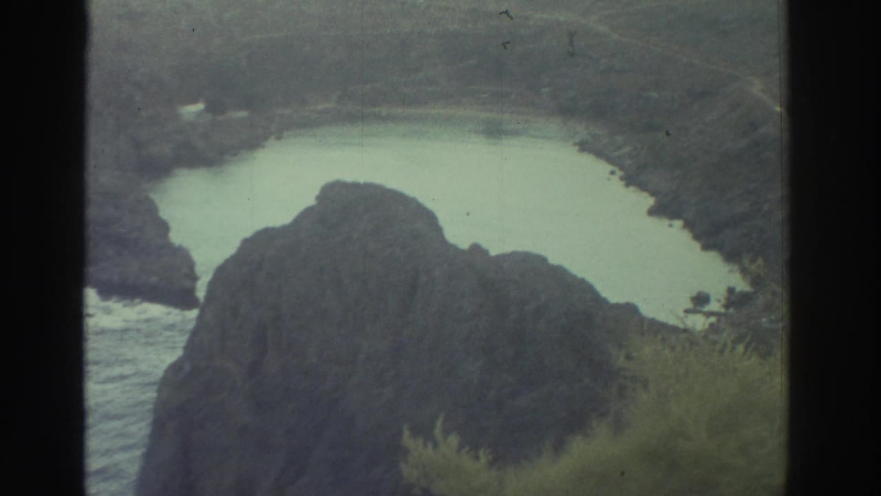 Coastal water curves around a large dark rock with greenery at the edge.