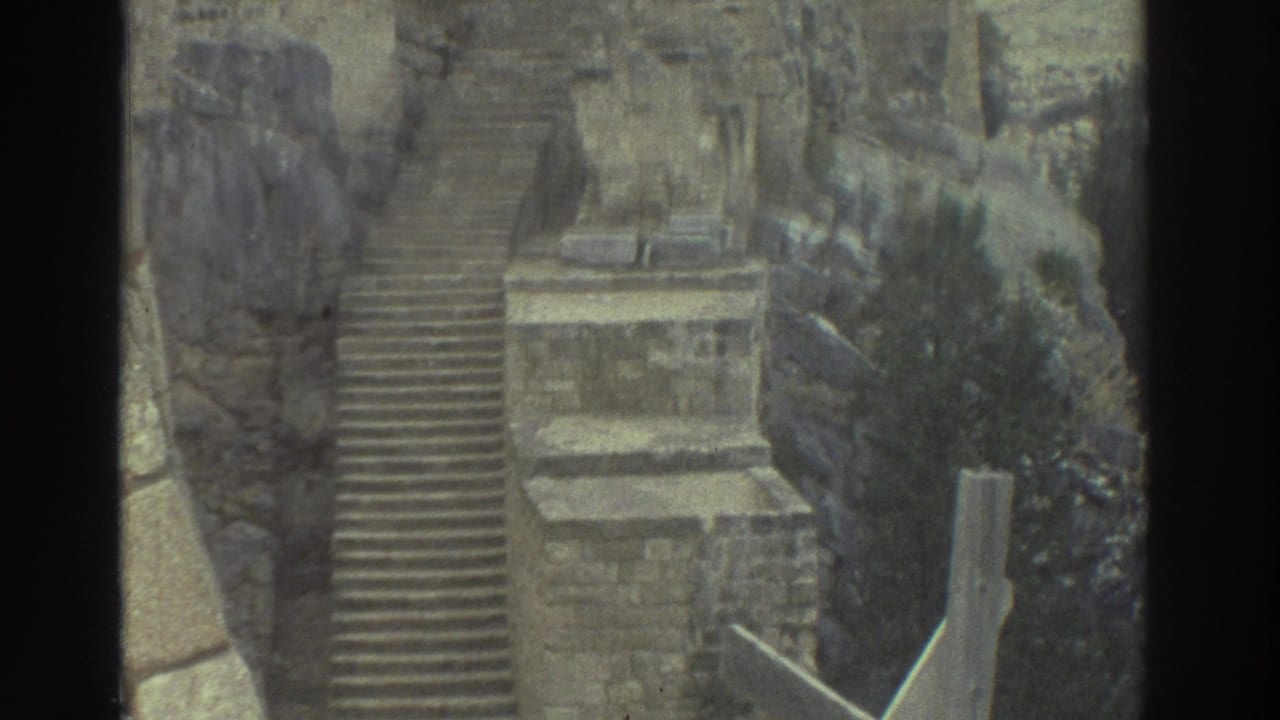 1976 Greece 8mm frame showing a steep stone staircase, rough masonry, rocky hillside, and a small landing within castle ruins.