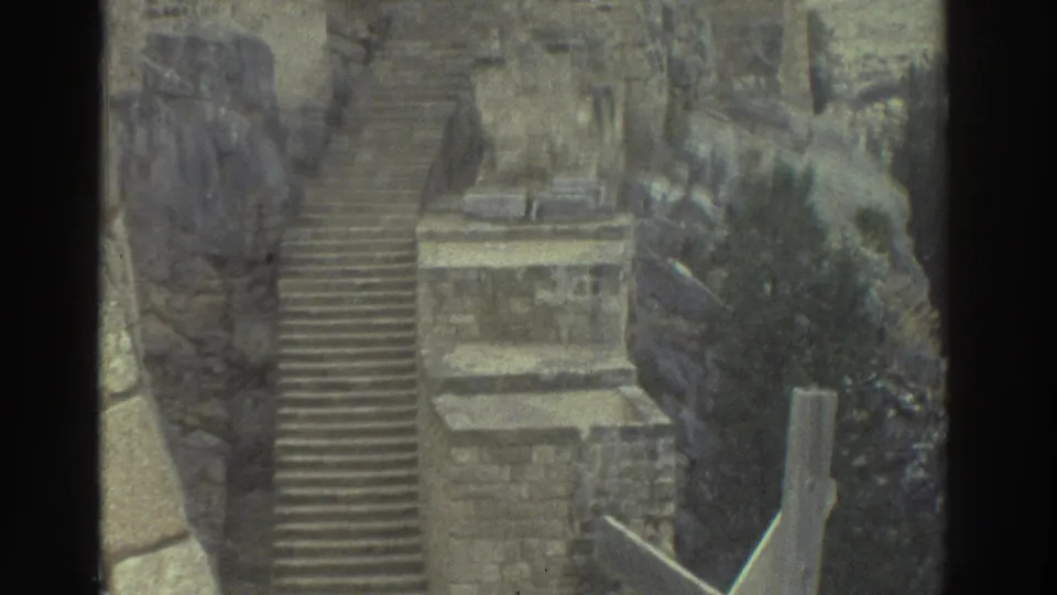 1976 Greece 8mm frame showing a steep stone staircase, rough masonry, rocky hillside, and a small landing within castle ruins.