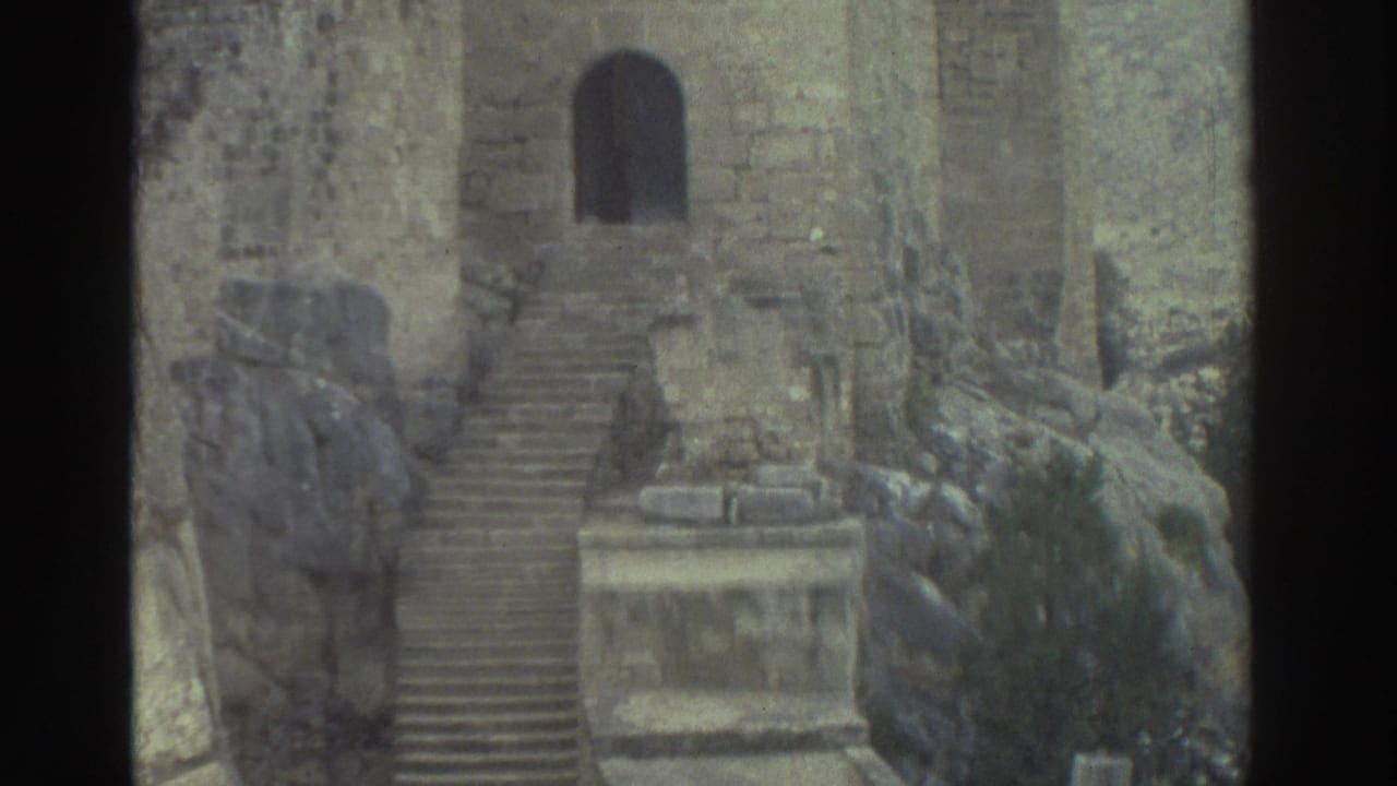1976 Greece 8mm frame with an arched doorway, long stone steps, rough block walls, rocky outcrop, and vegetation in castle ruins.