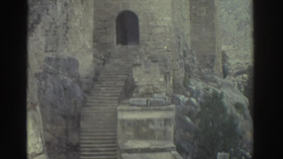 1976 Greece 8mm frame with an arched doorway, long stone steps, rough block walls, rocky outcrop, and vegetation in castle ruins.