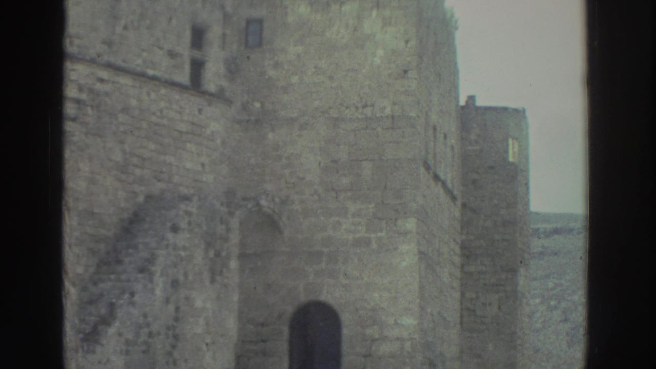 Stone village wall and arched doorway beside a narrow cobblestone lane.