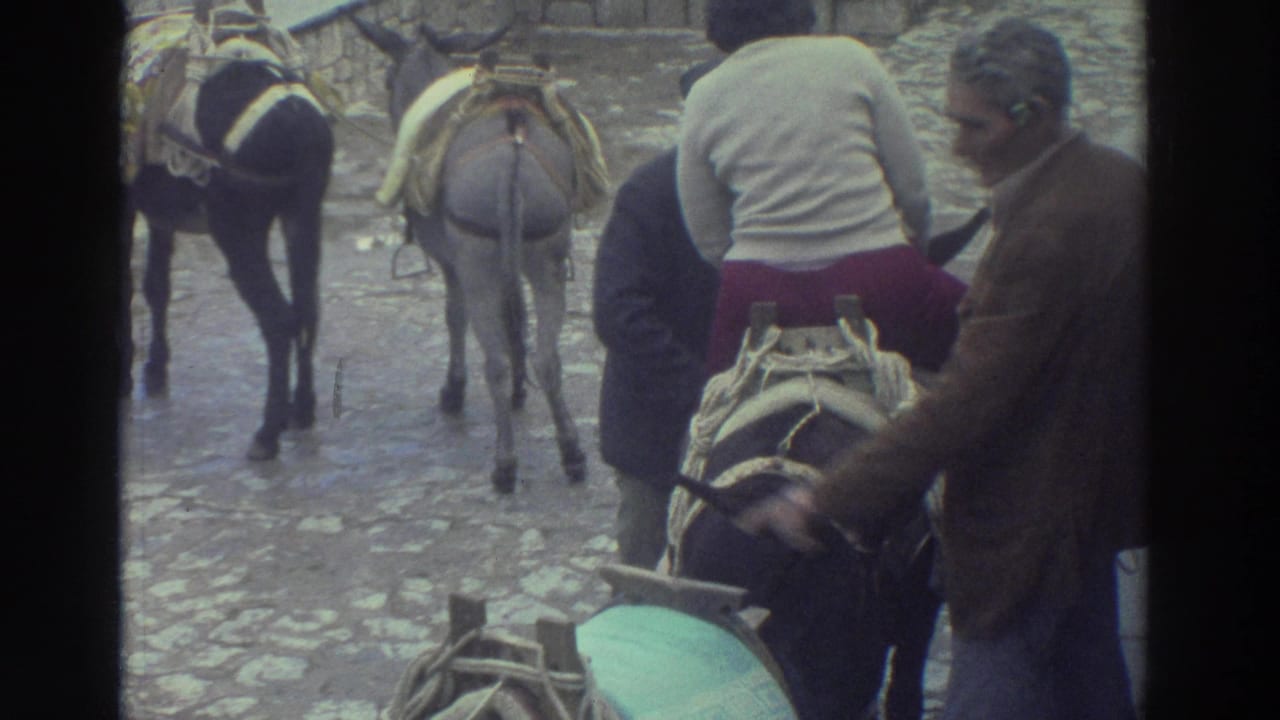 1976 Greece travel footage frame with a seated rider and men adjusting or steadying a saddled donkey or burro.