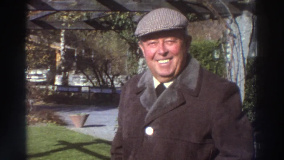 Older man smiles toward the camera in a garden, consistent with the supplied 1976 Greece home-movie context.