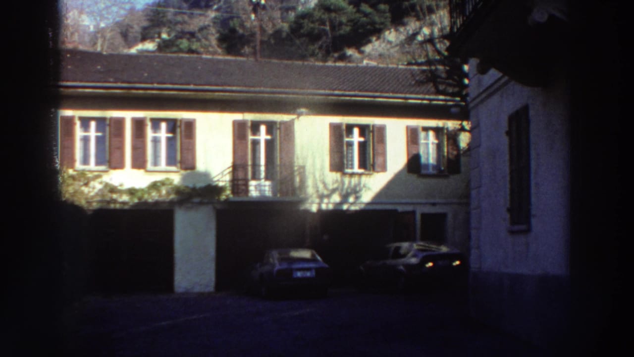 Residential facade with brown shutters, a garage, and two parked cars near the building.