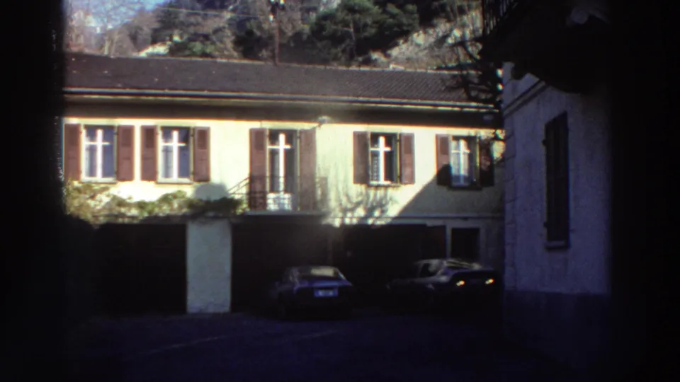 1976 Greece street view of a shuttered home with garage openings and parked classic cars in front.