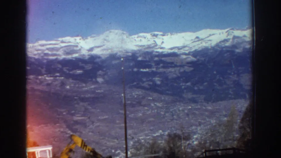 1976 Greece 8mm frame of snow-capped mountains overlooking a valley, with a foreground pole and visible light leak from the film scan.