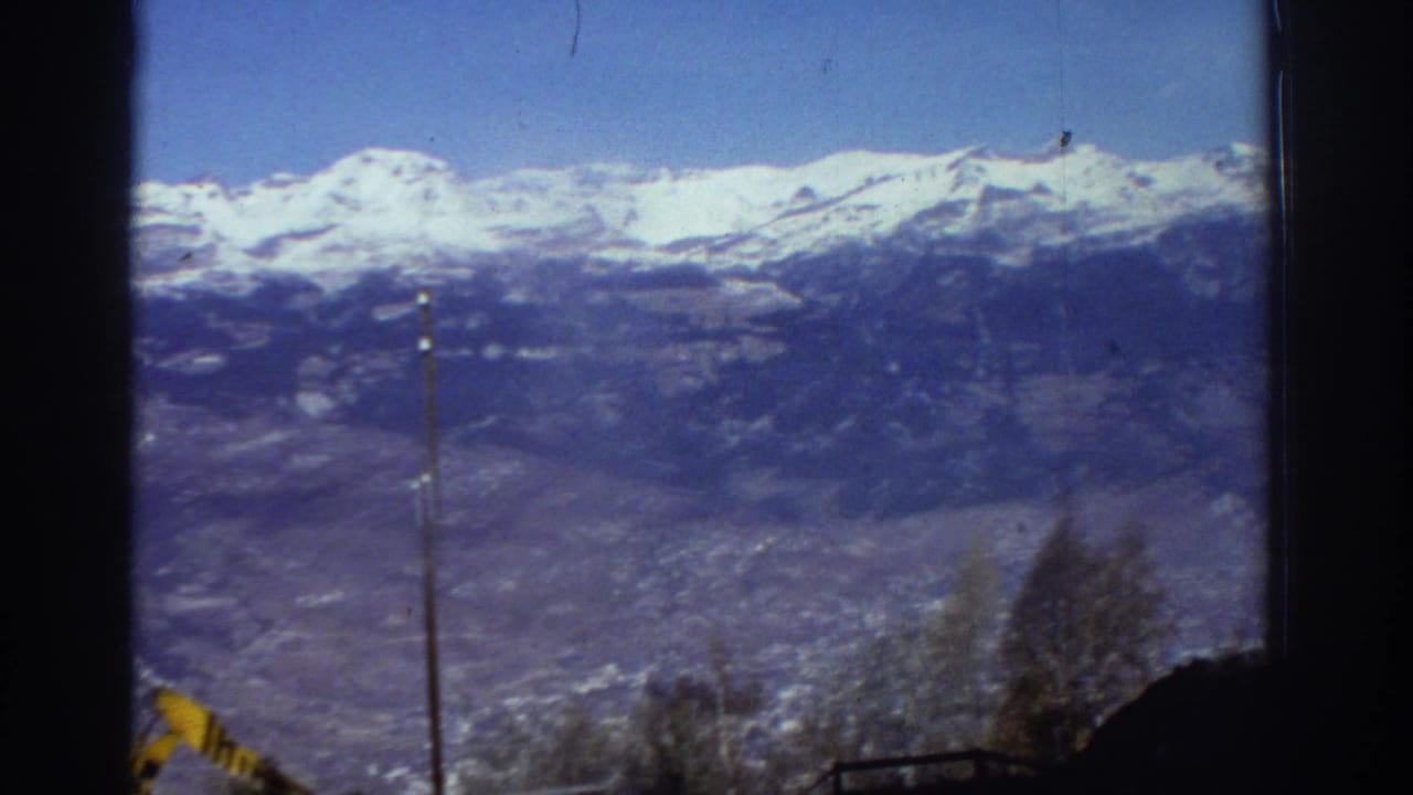 1976 Greece 8mm frame showing a snow-covered mountain ridge, valley below, bare trees, and a dark window or film border.