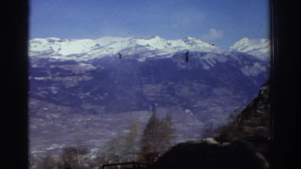 1976 Greece 8mm view across snow-topped mountains and a broad valley, partly obscured by dark vertical borders.