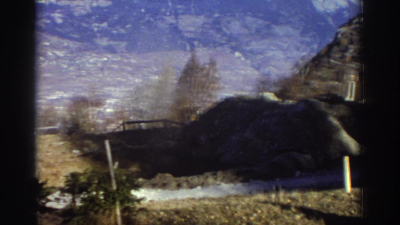 1976 Greece winter landscape with snow-dusted mountains, roadside posts, bare trees, and dark construction earth in the foreground.