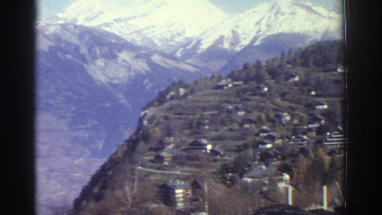 Mountain valley with a hillside village and snowy peaks beyond.