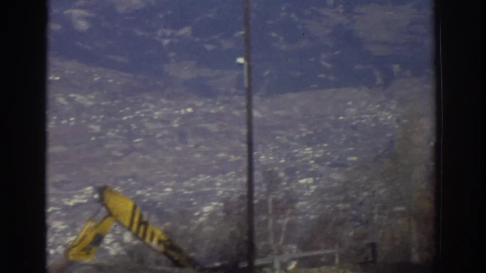 1976 Greece 8mm view of a distant valley town with a foreground pole and small yellow object near the lower edge.
