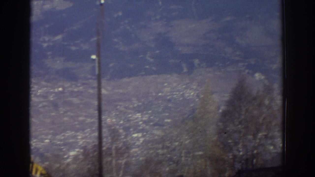 Snow-capped mountains and a valley town seen through a dark window frame.