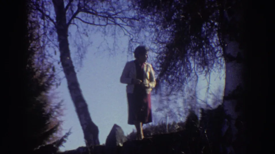 The woman remains framed by dark trees and pale sky in this 1976 Greece 8mm forest scene.