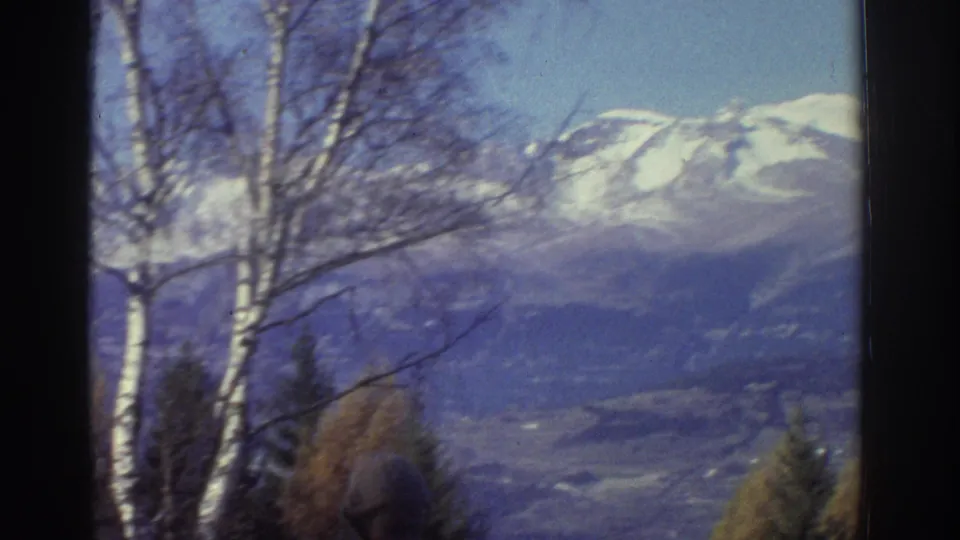 1976 Greece 8mm landscape view with white-barked trees in the foreground and snow-capped mountains across a hazy valley.
