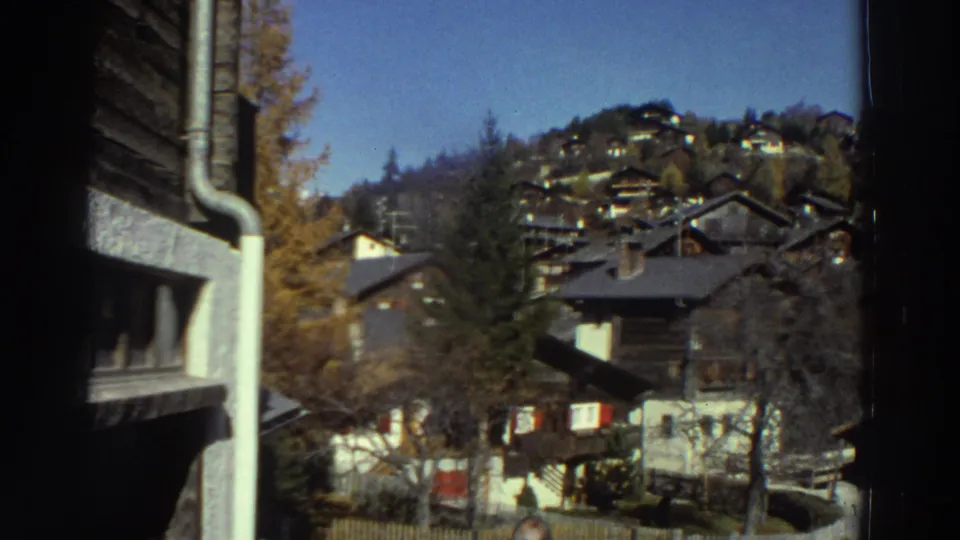 1976 Greece home-movie view of hillside houses, trees, fences, and a sloped residential street in bright daylight.