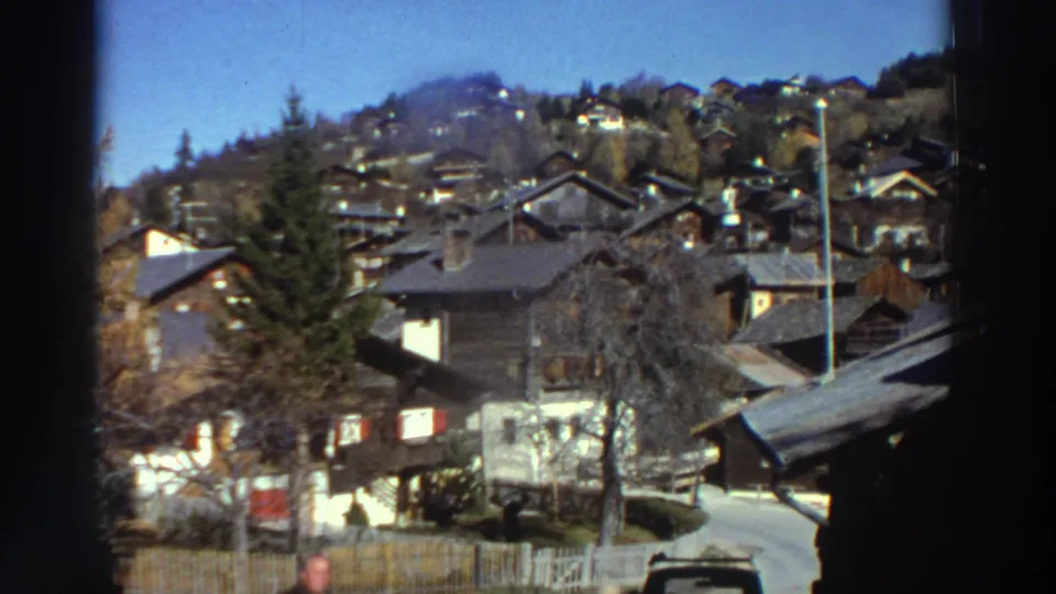 1976 Greece exterior view of hillside homes and trees, framed by dark 8mm gate edges during a slow pan.