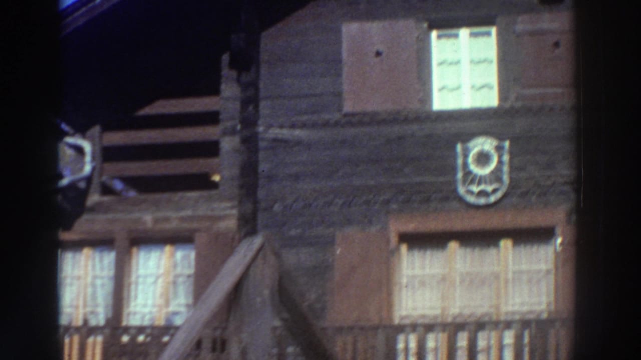 Upper wooden wall with bright window, shutters, balcony edge and circular emblem.