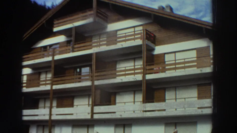 1976 Greece home-movie view of upper balconies, shuttered windows, and the steep roofline of a chalet-like building.