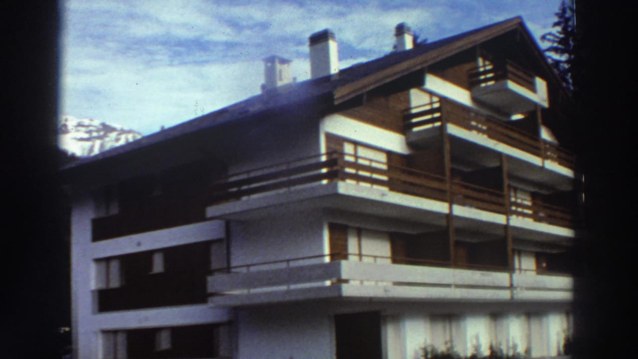 White chalet with wooden balconies below snowy mountains.