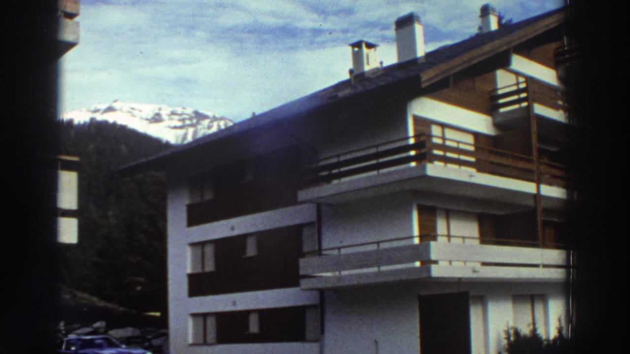 A 1976 Greece travel frame shows the chalet from a slightly different angle, with balconies, chimneys, trees, and snowy peaks visible.