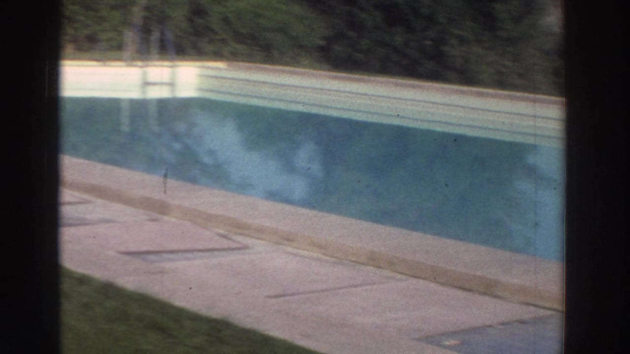 1976 Greece 8mm frame showing a swimming pool, concrete deck, lawn, hedge, and part of a golf-course view.