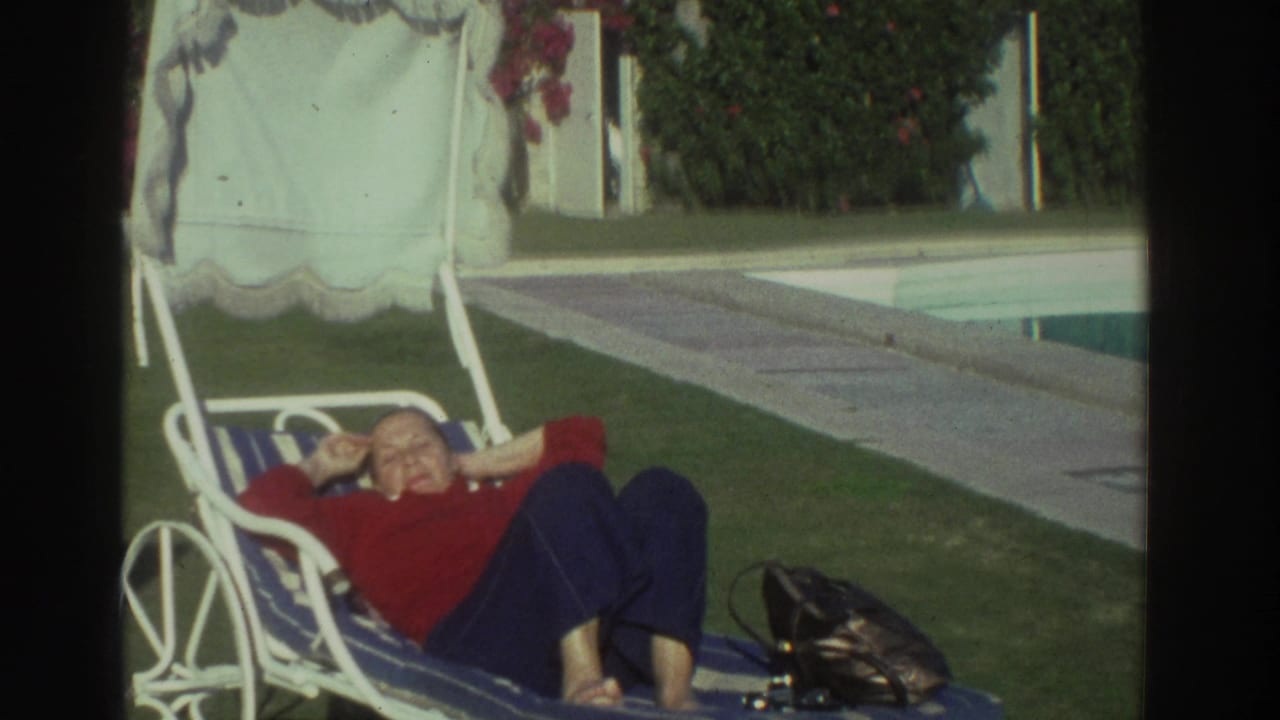 1976 Greece 8mm frame of a woman in a red sweater resting on a striped lounge chair near a pool with a handbag nearby.