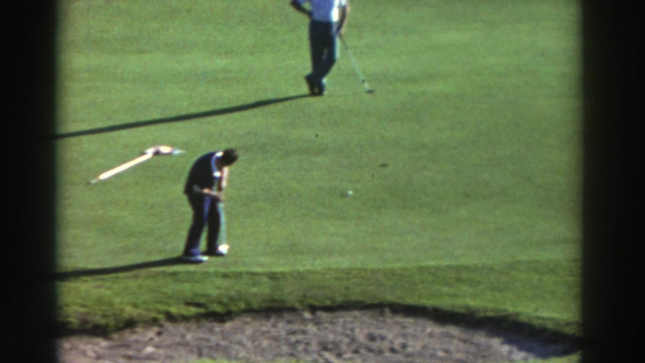 1976 Greece 8mm frame with one man putting on the green and another standing nearby, with a sand bunker visible along the lower edge.