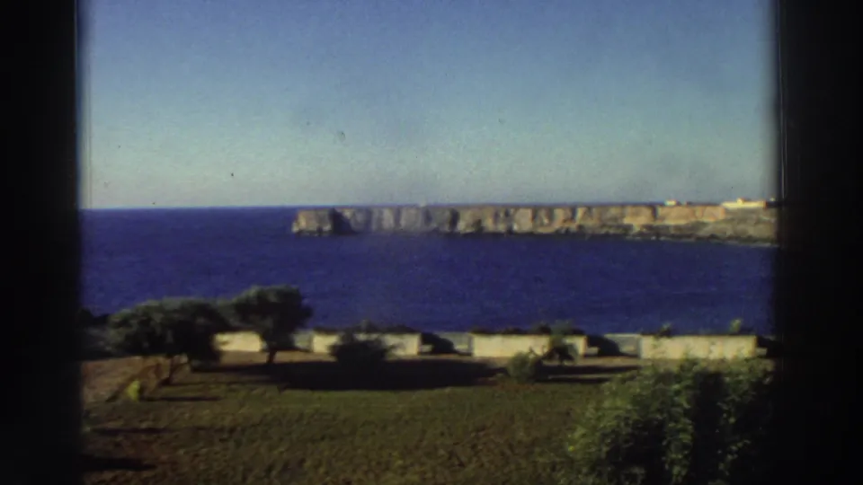 The final 1976 Greece frame shows a dark-framed seaside vista with blue water, pale cliffs, trees, and low walls in the foreground.