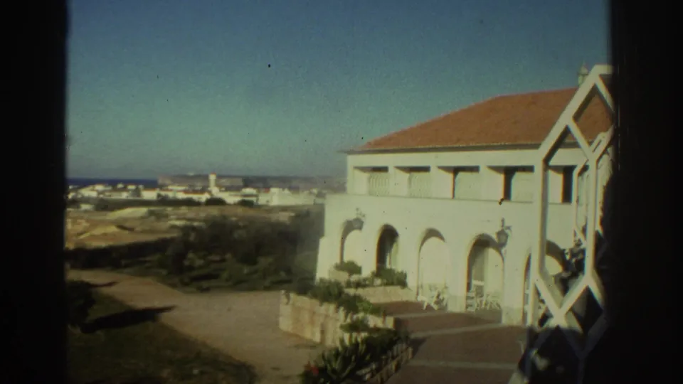 1976 Greece home-movie frame showing a large white building with arches and a terracotta roof above the coast.