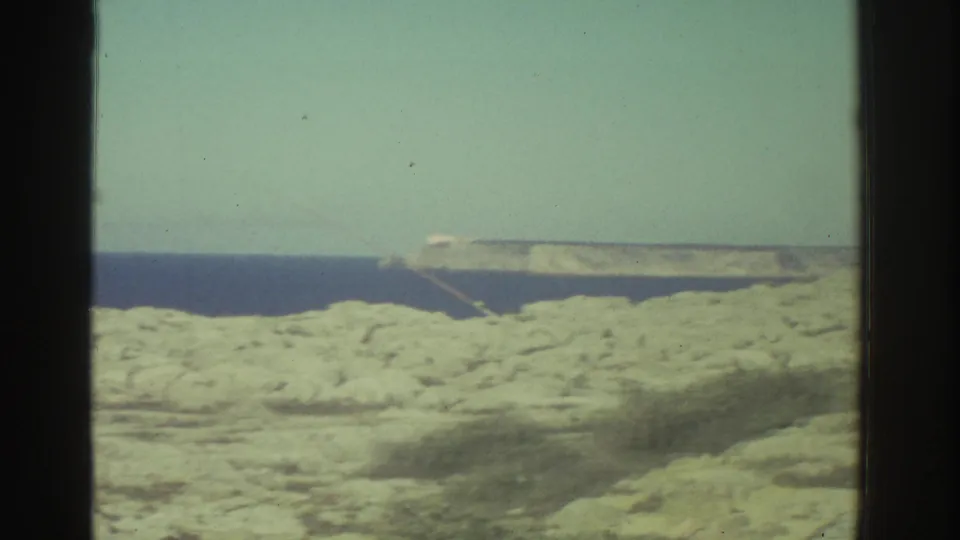The final frame shows Greece coastal rocks and sea with a pale horizontal apparatus or structure crossing the background in soft Super 8 color.