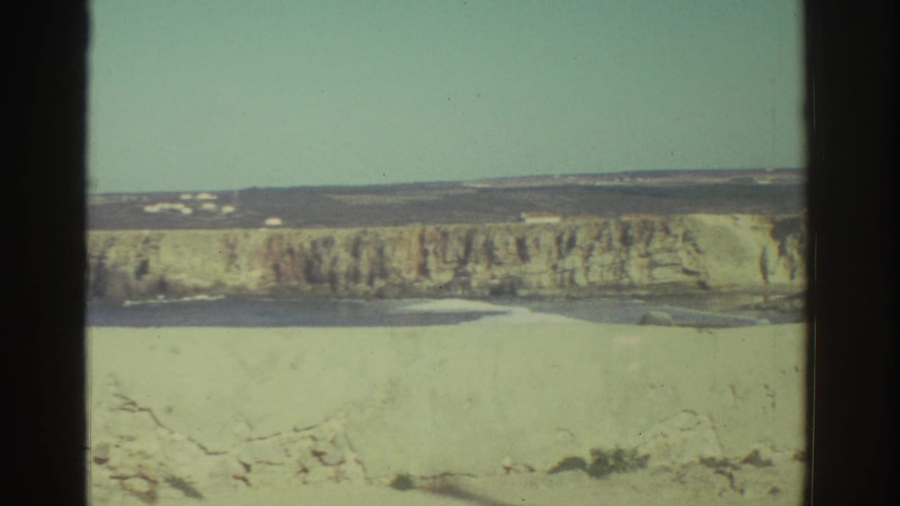 Wide view of a pale wall or cliff line with distant buildings and open sky.