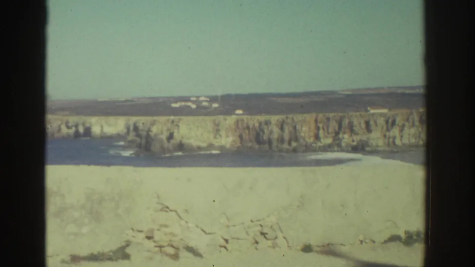1976 Greece 8mm frame showing a distant sunlit landscape, pale stone or cliff face, low buildings, and soft home-movie focus.