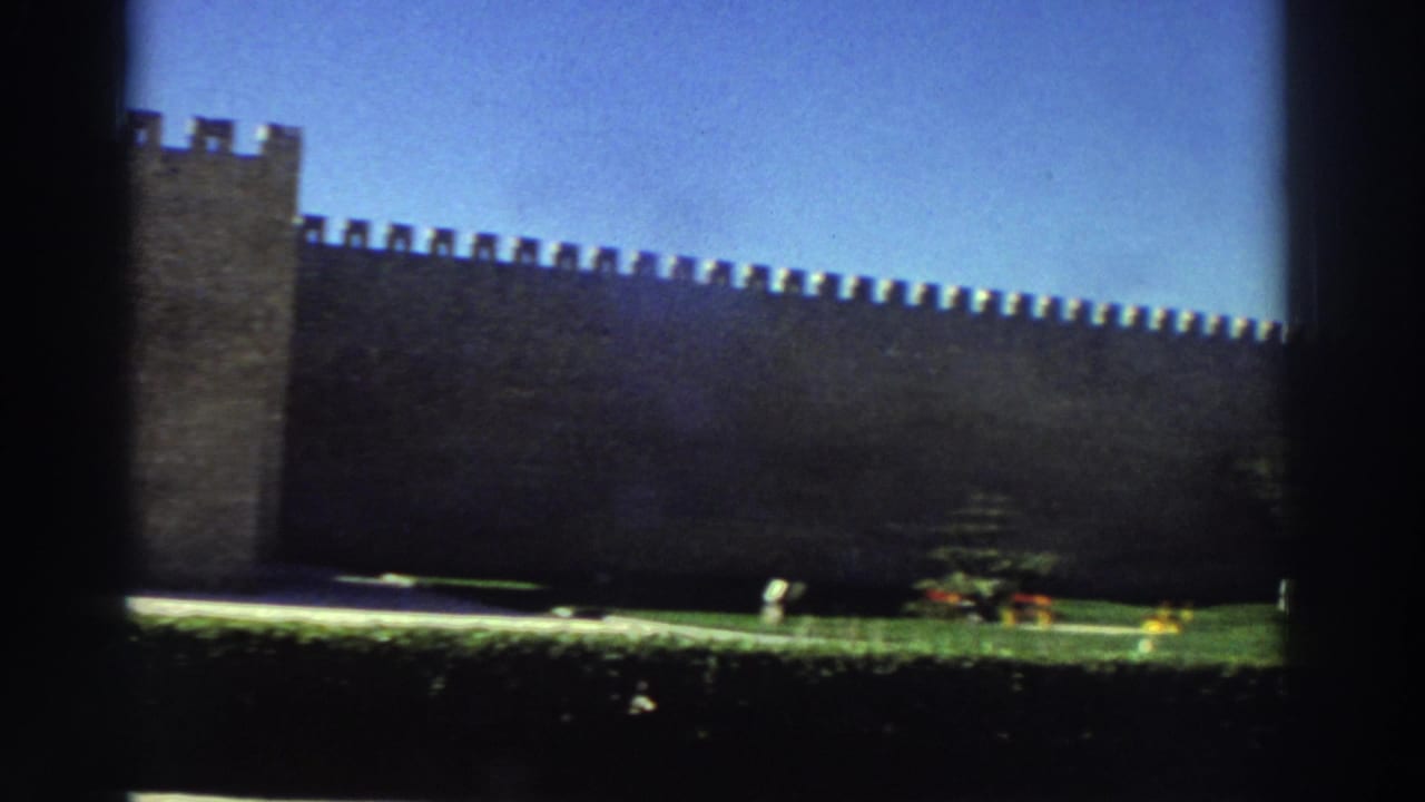 1976 Greece 8mm frame of a long crenellated fortress wall and tower above a green lawn, with small distant visitors near the grounds.