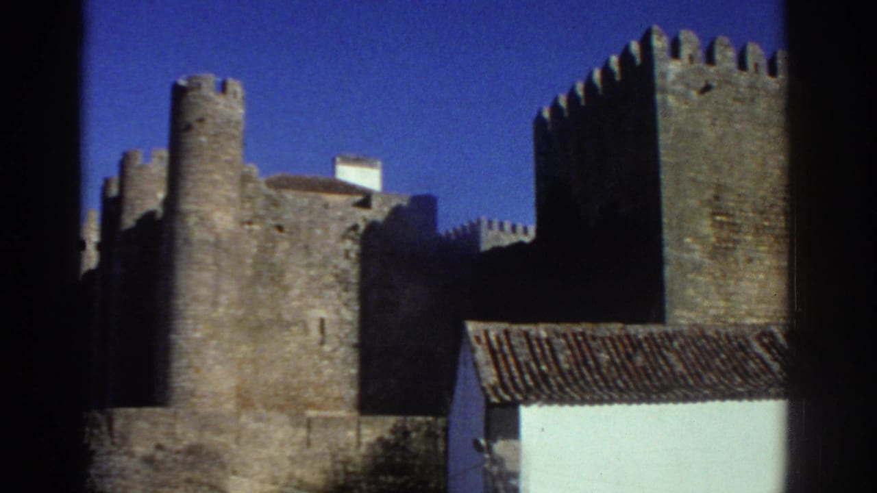 1976 Greece 8mm frame showing medieval stone castle towers and crenellated walls behind a white foreground house.