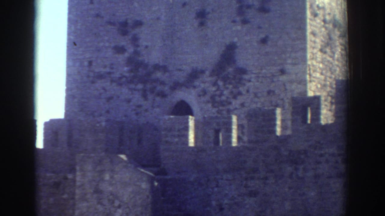1976 Greece 8mm frame showing a castle-like stone tower with battlements and an arched opening.