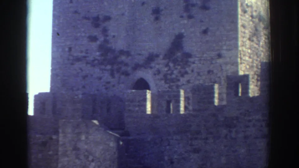 1976 Greece 8mm frame showing a castle-like stone tower with battlements and an arched opening.