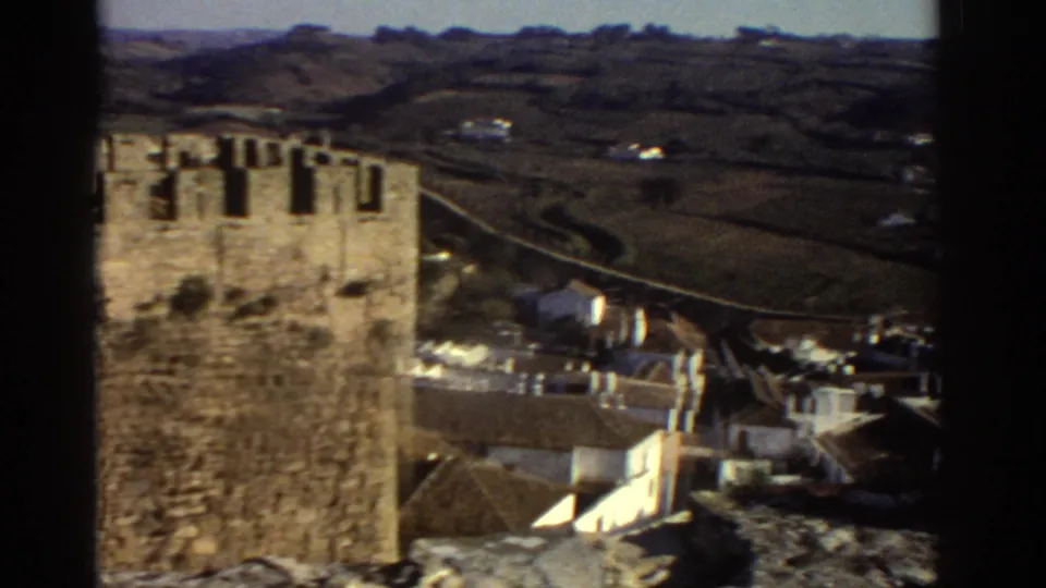 A Greek hillside village and stone tower are seen from the castle walls in soft 1970s 8mm color.