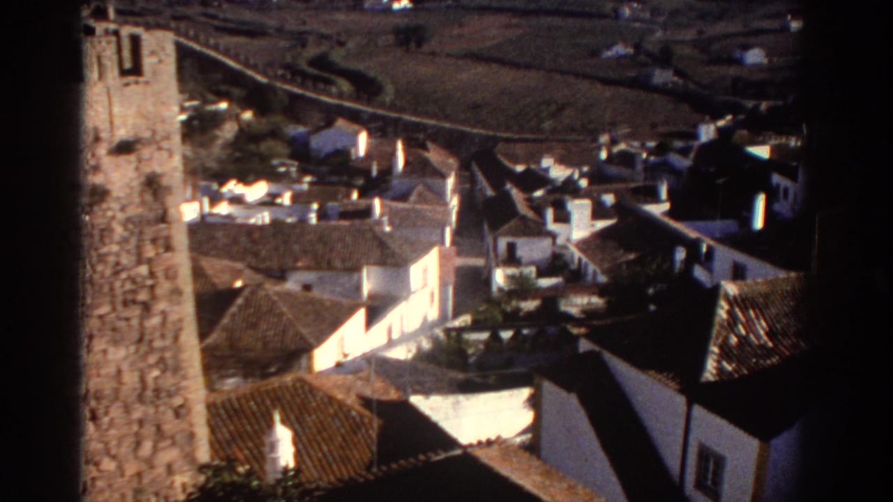 1976 Greece home-movie frame showing whitewashed houses, terracotta roofs, and a rough stone tower edge from above.