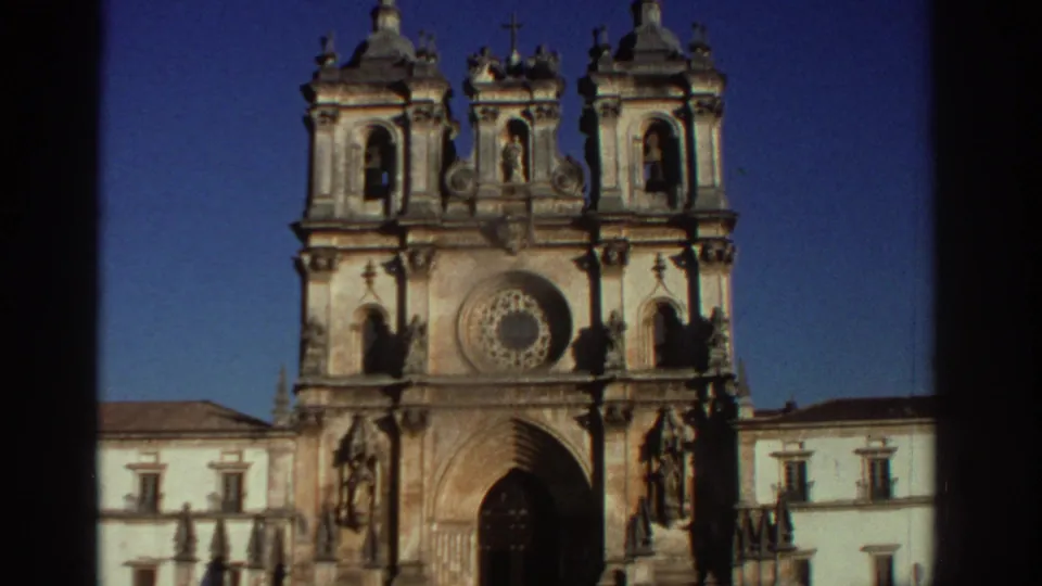1976 Greece 8mm frame of the cathedral front, with twin towers, a central rose window, statues, and adjoining pale buildings.
