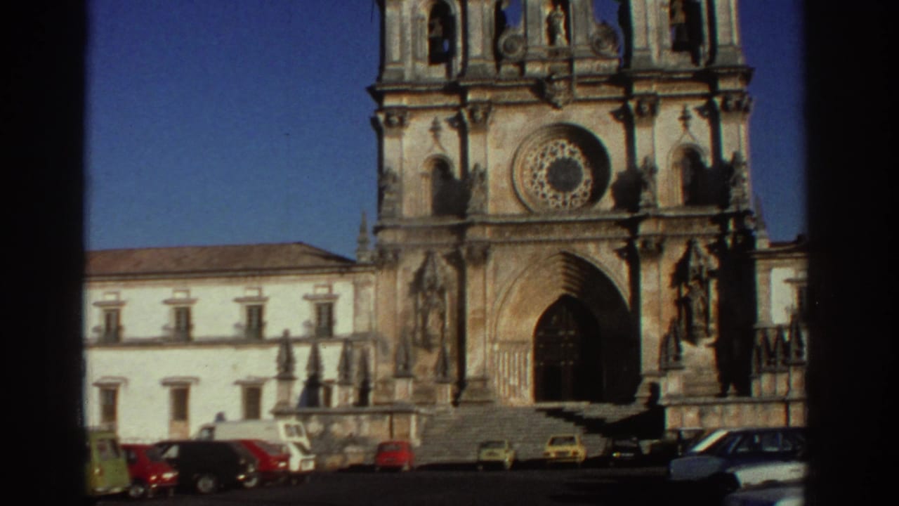 1976 Greece home-movie frame showing a grand stone cathedral facade, rose window, arched doorway, and compact cars parked across the square.