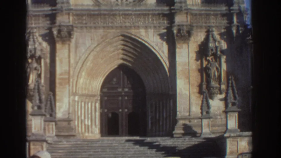 Closer 8mm view of the cathedral entrance in Greece, showing the pointed arch, carved stone details, dark doorway, and broad steps.