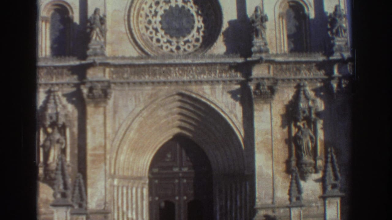 1976 Greece 8mm frame showing a stone cathedral facade with a pointed arched doorway, rose window, niches, and carved figures.