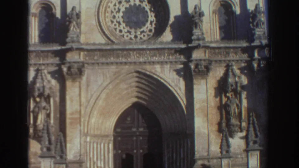1976 Greece 8mm frame showing a stone cathedral facade with a pointed arched doorway, rose window, niches, and carved figures.