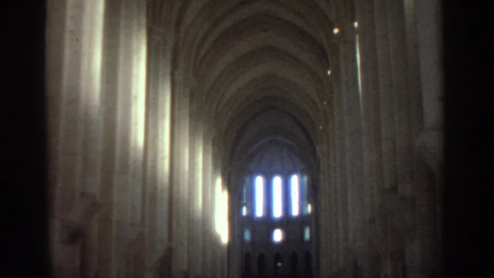 A closer 8mm view down the cathedral nave shows stone arches, side columns, and bright vertical windows at the end of the space.